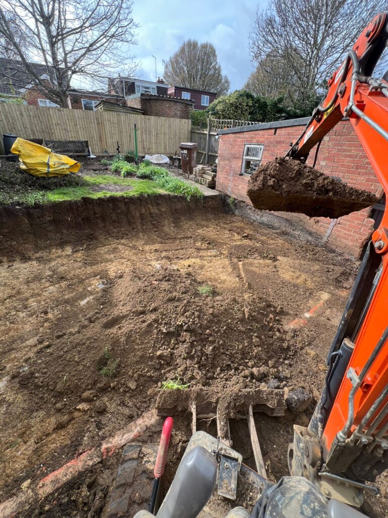Hitachi mini digger lifting a full bucket of spoil on a man and digger groundwork job in Newton Leys, Milton Keynes.