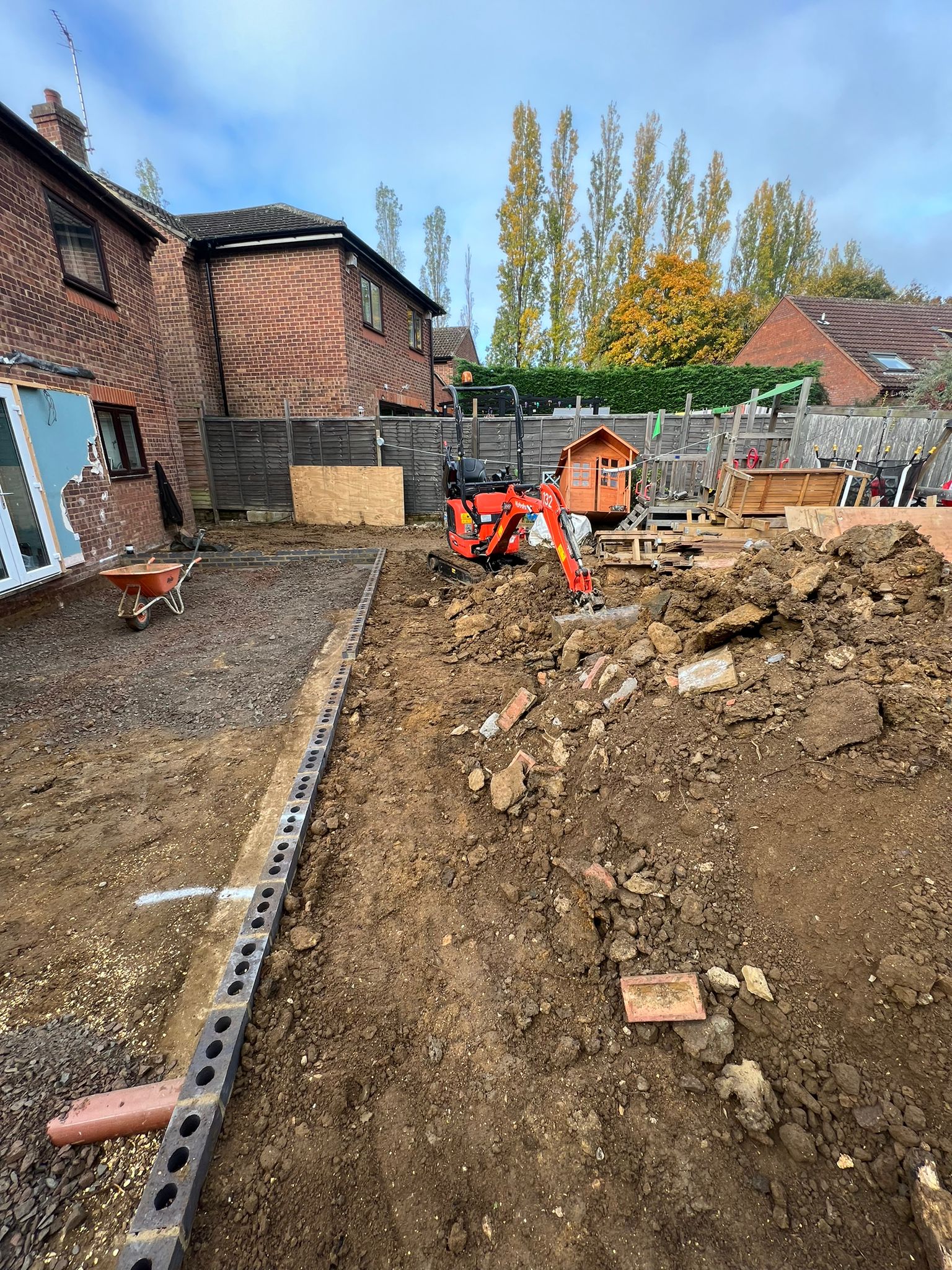 Operated mini digger clearing and levelling a back garden, with a wheelbarrow and new edging laid, on a man and digger groundwork job.